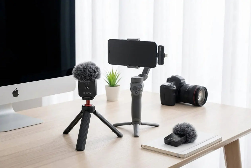 Camera equipment on a desk with a computer monitor and plant in the background